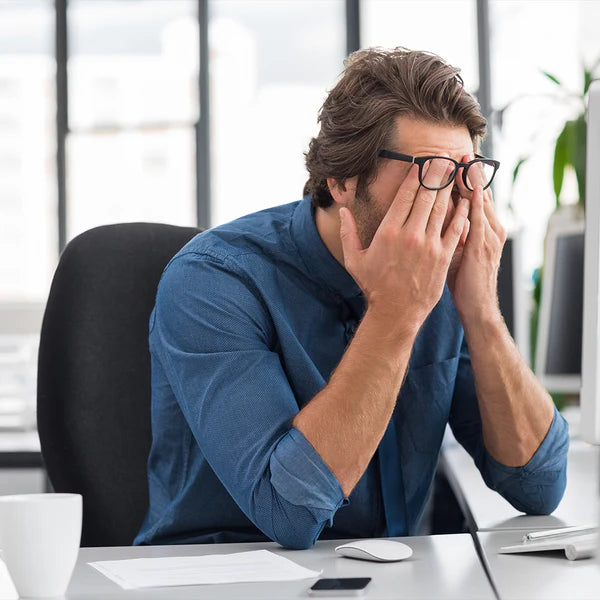 Man rubbing eyes at office desk, looking stressed