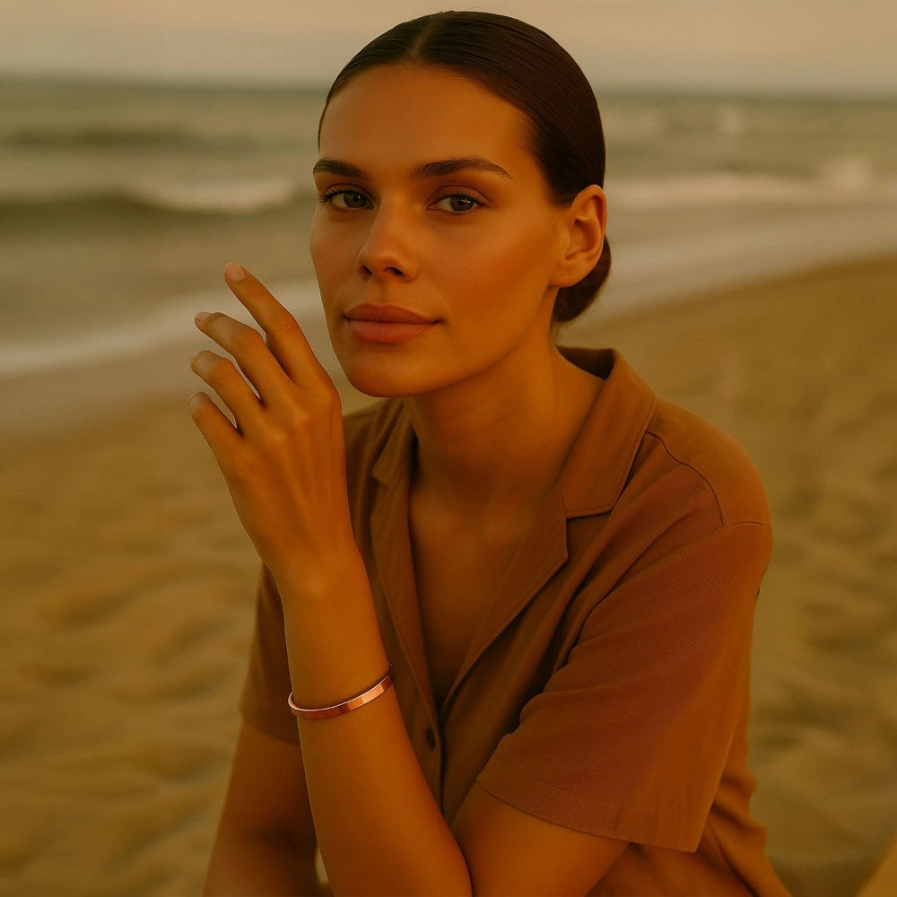 Smiling woman in a brown outfit sitting by the seaside wearing a rose gold Omlezo Magnetic Copper Bracelet